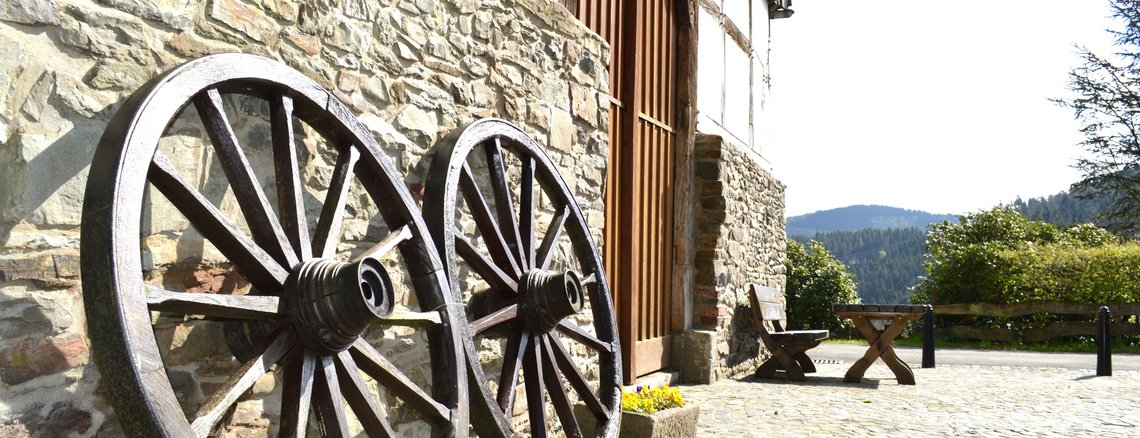 Vorplatz historisches Bauernhaus mit zwei alten Holzrädern und einer Holzbank mit Tisch