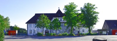 Panoramaufnahme im Frühling von der Grundschule Spormecke mit Schulhof, Bushaltestelle und daran angrenzendem Feuerwehrgebäude