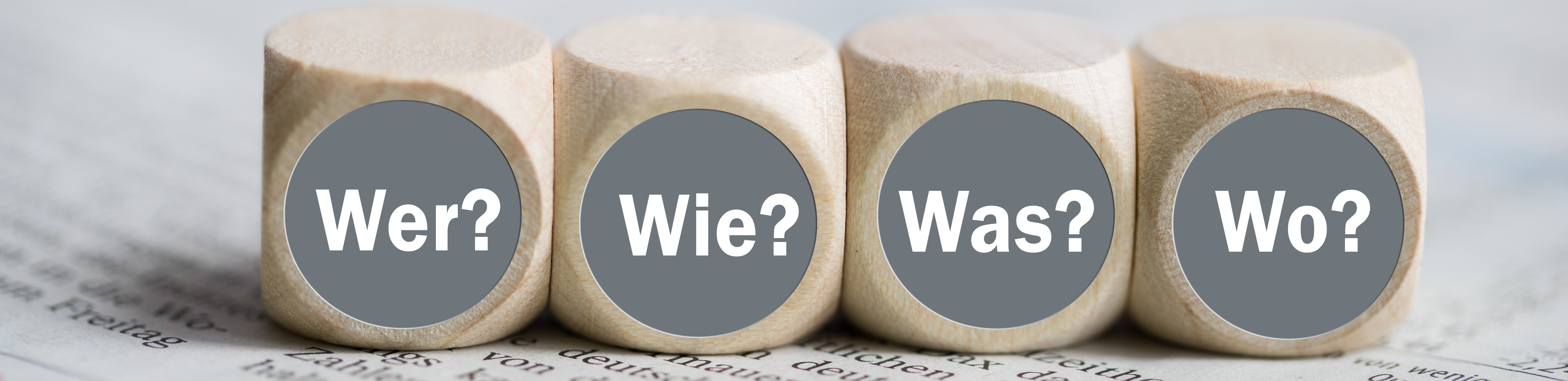 4 Würfel mit der Aufschrift Wer Wie Was Wo auf einer Zeitung