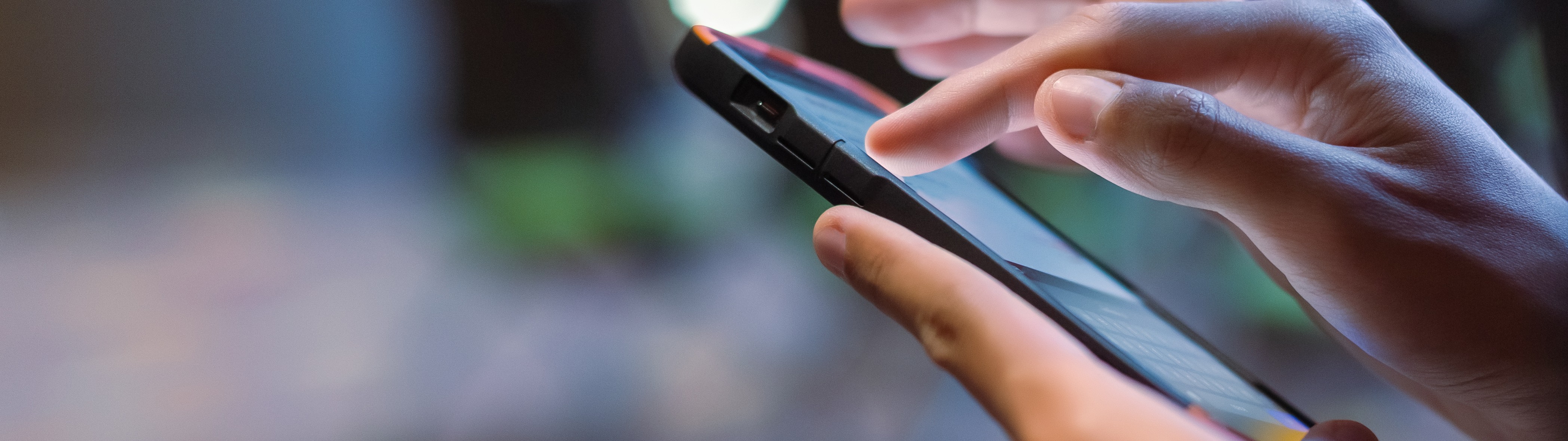 Nahaufnahme einer Männerhand, die in einem Besprechungsraum vor unscharfem Bokeh-Hintergrund ein Smartphone benutzt