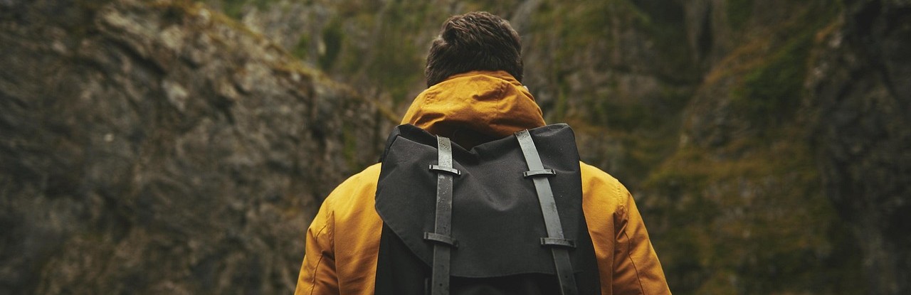 Wanderer umgeben von Felsen mit einer gelben Jacke und Rucksack